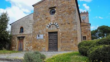 Un bâtiment historique en pierre, doté d’une tour horloge, d’une entrée centrale en arc de cercle et d’un clocher.