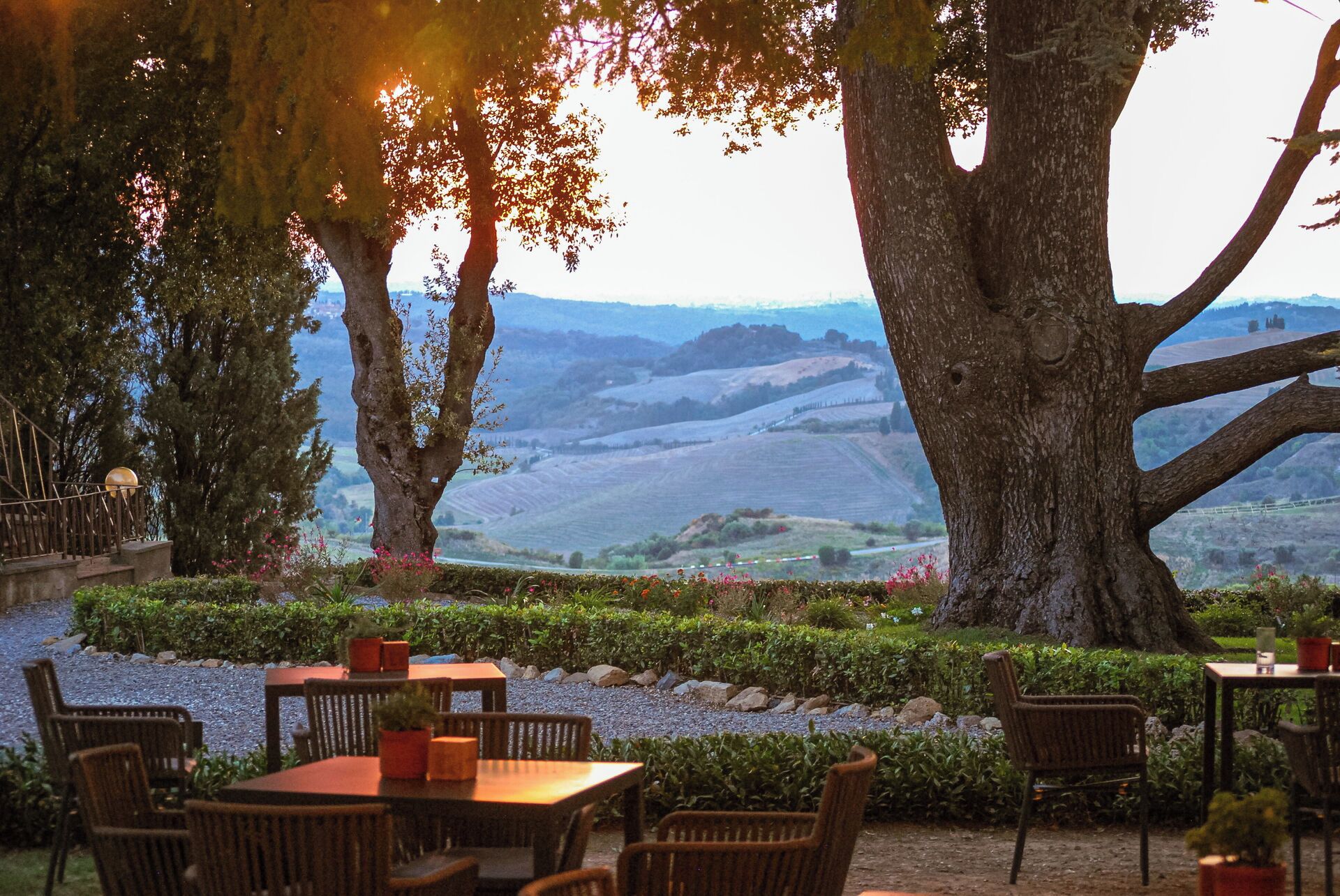 An outdoor seating area with tables and chairs, surrounded by trees and a view of rolling hills.