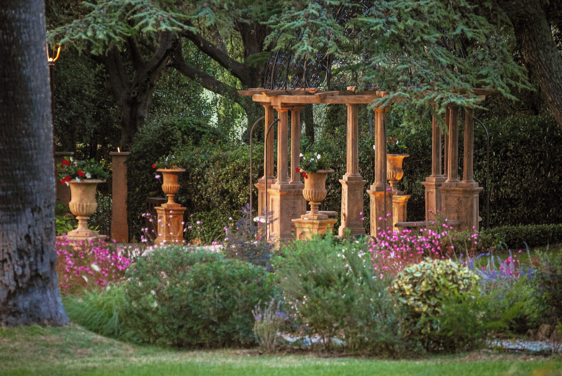 Un jardin agrémenté d’une pergola, entouré d’une végétation luxuriante et de plantes en fleurs.