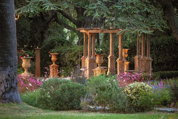 A garden with a pergola structure, surrounded by lush greenery and flowering plants.