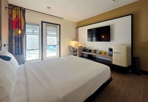 A hotel room with a large bed, a desk with a chair, a television, and a minibar. - Pool + Spa + Firepit + Courtyard | Mtn Views | Sun Queen at Mahala (Palm Springs)