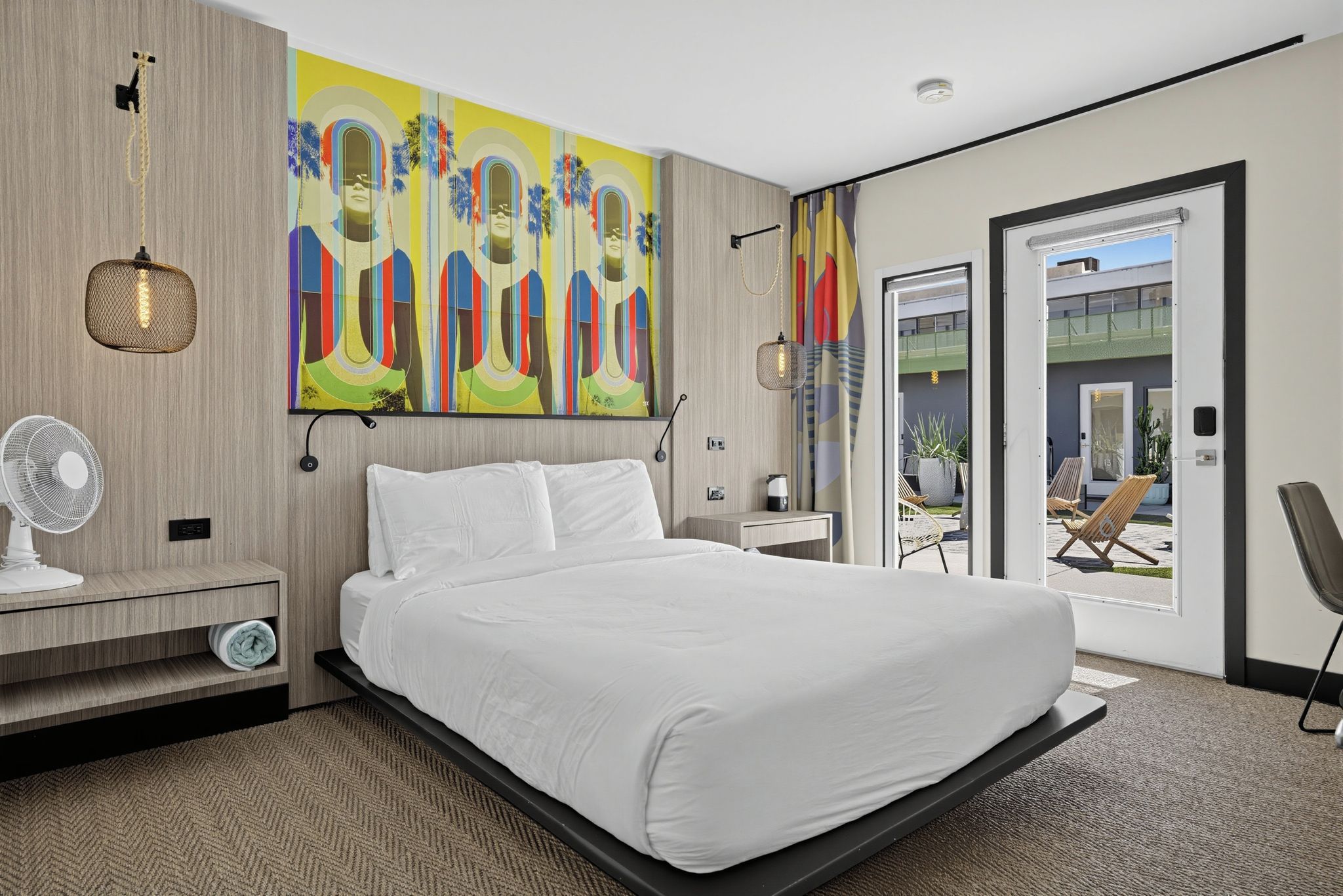 Une chambre d’hôtel moderne dotée d’un grand lit, d’un téléviseur à écran plat, d’une table de chevet, d’une chaise et donnant sur le balcon extérieur.