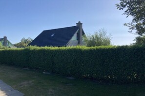 Una casa amb teulada inclinada, envoltada per un bord ple de vegetació.