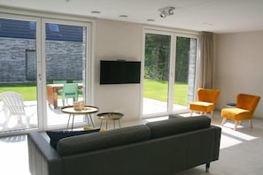 Una sala de estar con un sofá, dos sillones, un televisor y un ventanal corredizo que da a un patio.