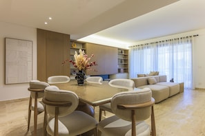 Una sala de estar moderna con una mesa de comedor de vidrio rodeada de sillas, un sofá y un jarrón decorativo con flores.