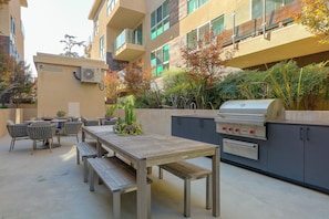 Eine Terrasse im Freien mit Holztisch und -stühlen, einem Grill und Kübelpflanzen.