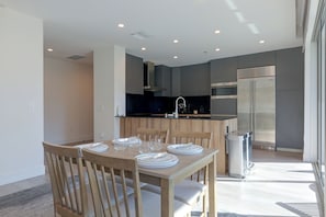 A modern kitchen with a dining area, featuring a stainless steel refrigerator, a built-in oven, and a black countertop. - Walkable & Sleek LA Condo w/ Private Office (Los Angeles)