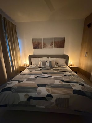 Una habitación de hotel con una cama grande, una mesita de noche con una lámpara y una pared con tres cuadros enmarcados.