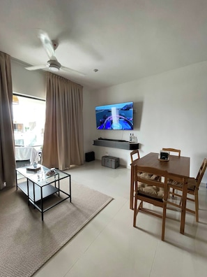 Una sala de estar con televisión, ventilador de techo, mesa de comedor y mesa de centro.