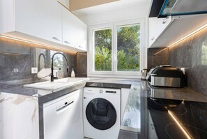Eine moderne Küche mit eingebauter Waschmaschine und Trockner, einem großen Fenster und Blick auf Grünflächen.