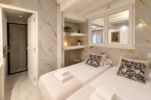 Ein Hotelzimmer mit zwei Betten, einer Dusche, einem Schminktisch mit Spiegel und einem kleinen Fenster mit einem Bild.