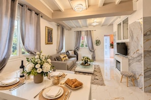Ein modernes Wohnzimmer mit Essbereich, einer Sofagarnitur, einem Fernseher und einem Kamin aus Marmor.