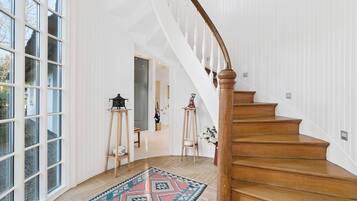 A spacious interior with a wooden staircase, large windows, and a patterned rug.