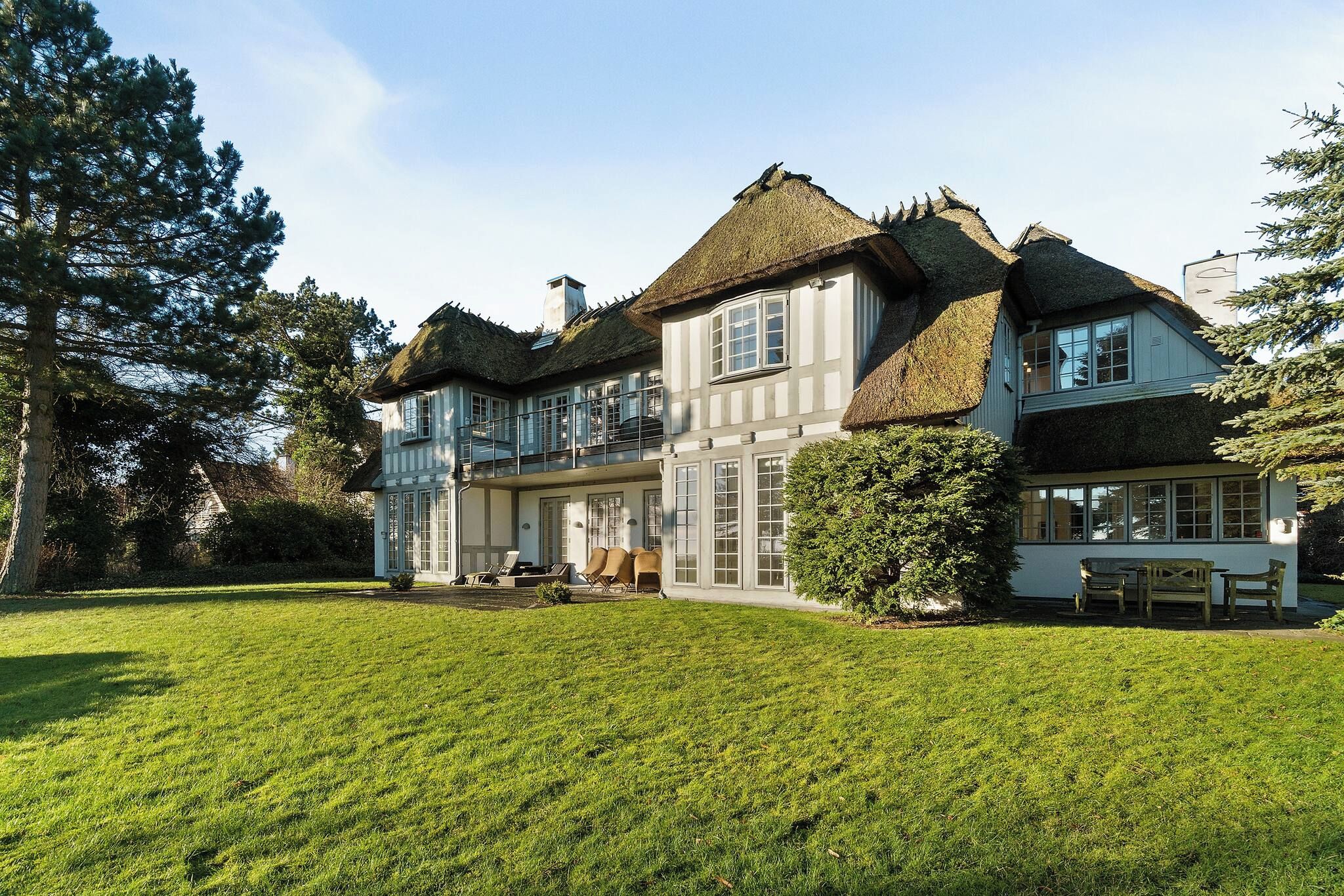 A large, two-story house with a thatched roof, a well-maintained lawn, and a seating area with outdoor furniture.