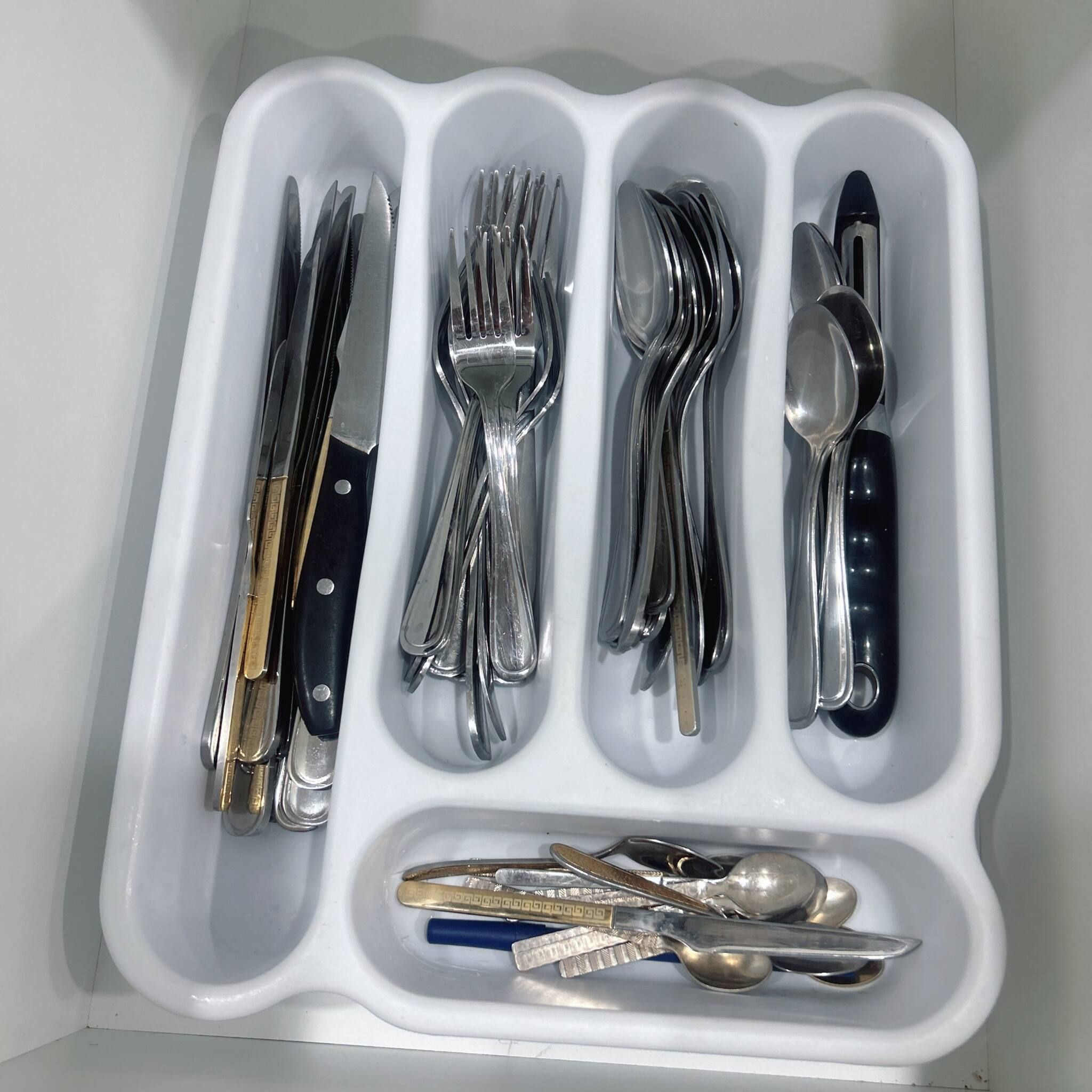 A white tray with various cutlery items including forks, knives, spoons, and a pair of scissors.