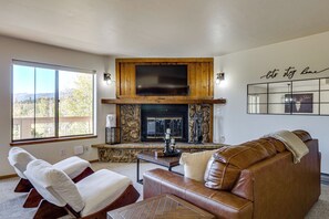 A living room with a stone fireplace, leather sofa, and a large window. - Hikes + Hot Tub Soaks! Extended Silverthorne Stay (Silverthorne)