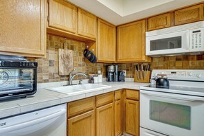 Una cocina con armarios de madera, microondas, horno, pileta y lavavajillas.