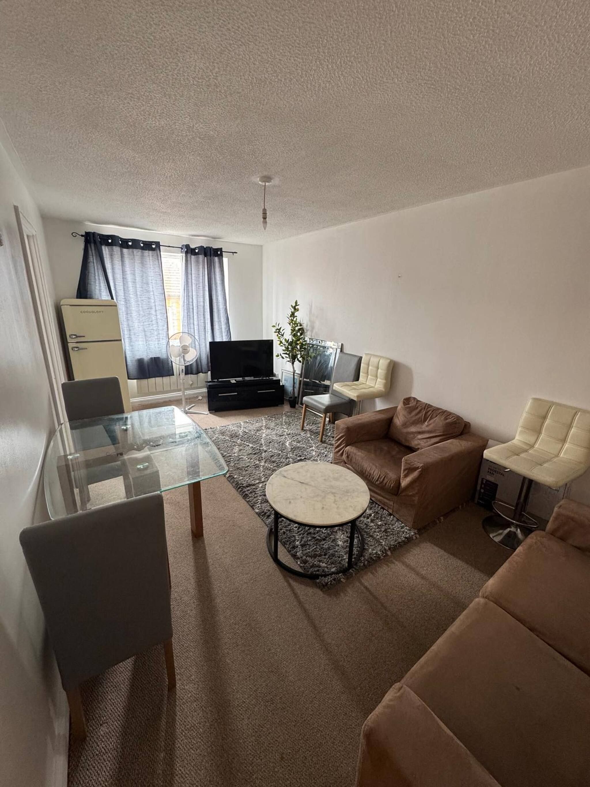 A compact living space with a glass dining table, a brown sofa, a television, and a small side table.