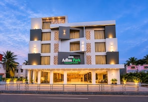 Un hôtel à plusieurs étages, doté d’une façade moderne, de grandes fenêtres et d’une enseigne indiquant qu’il s’agit de l’hôtel Adhis Park.