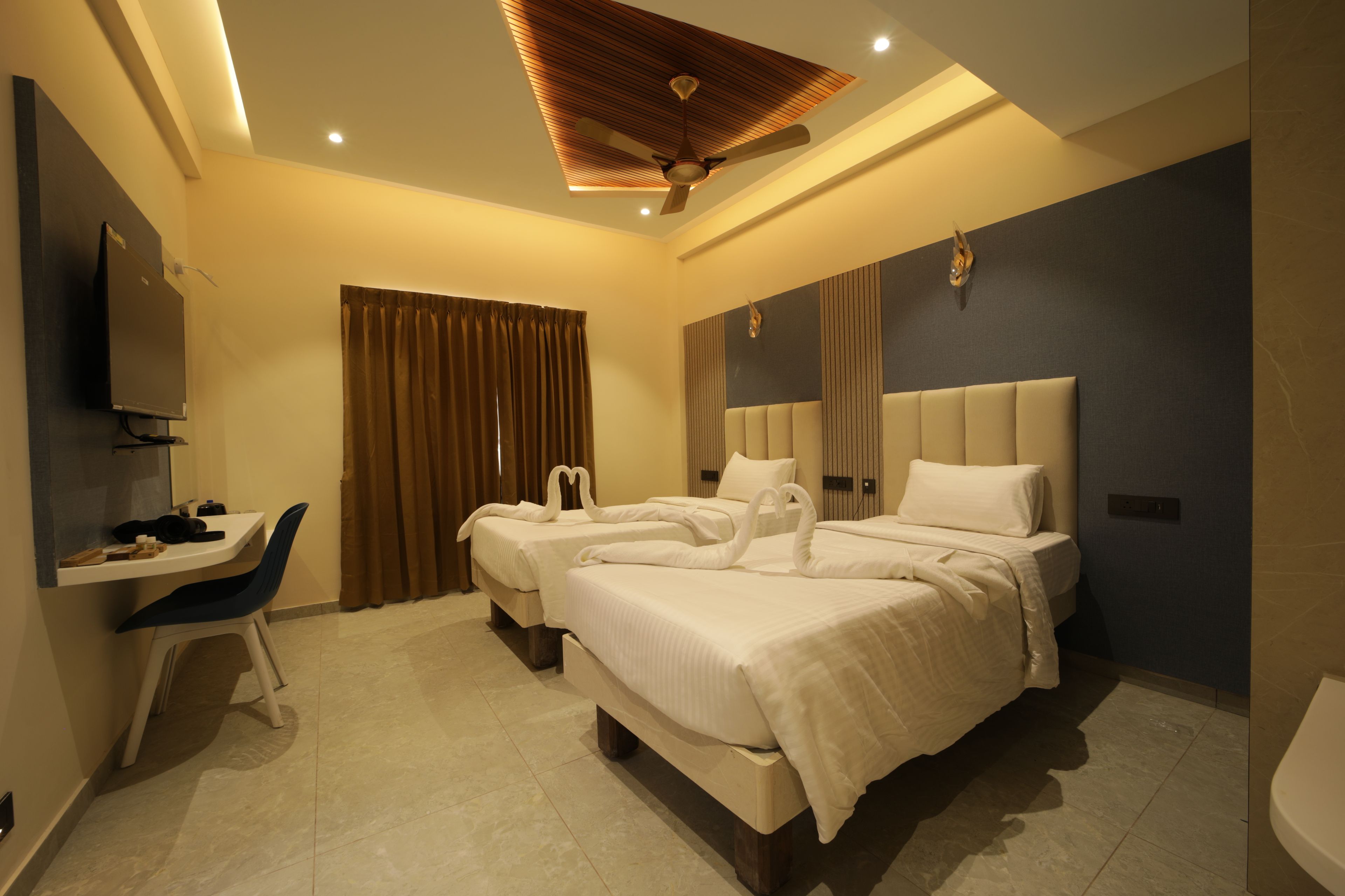 A hotel room with two beds, a desk, a chair, and a ceiling fan.