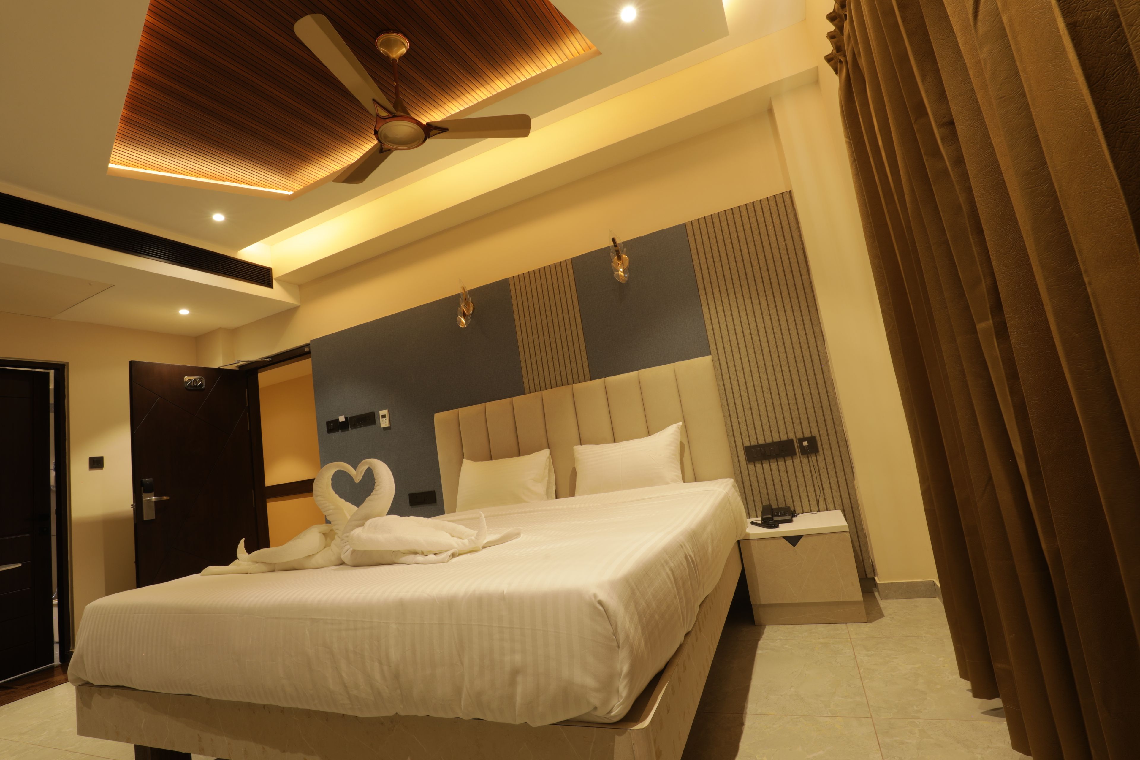 Quarto de hotel moderno com uma cama grande, um ventilador de teto e mesa de cabeceira com telefone.