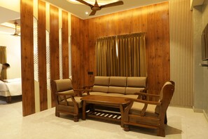 Una habitación con pared de paneles de madera, un sofá, dos sillones, una mesa de centro y un ventilador de techo.