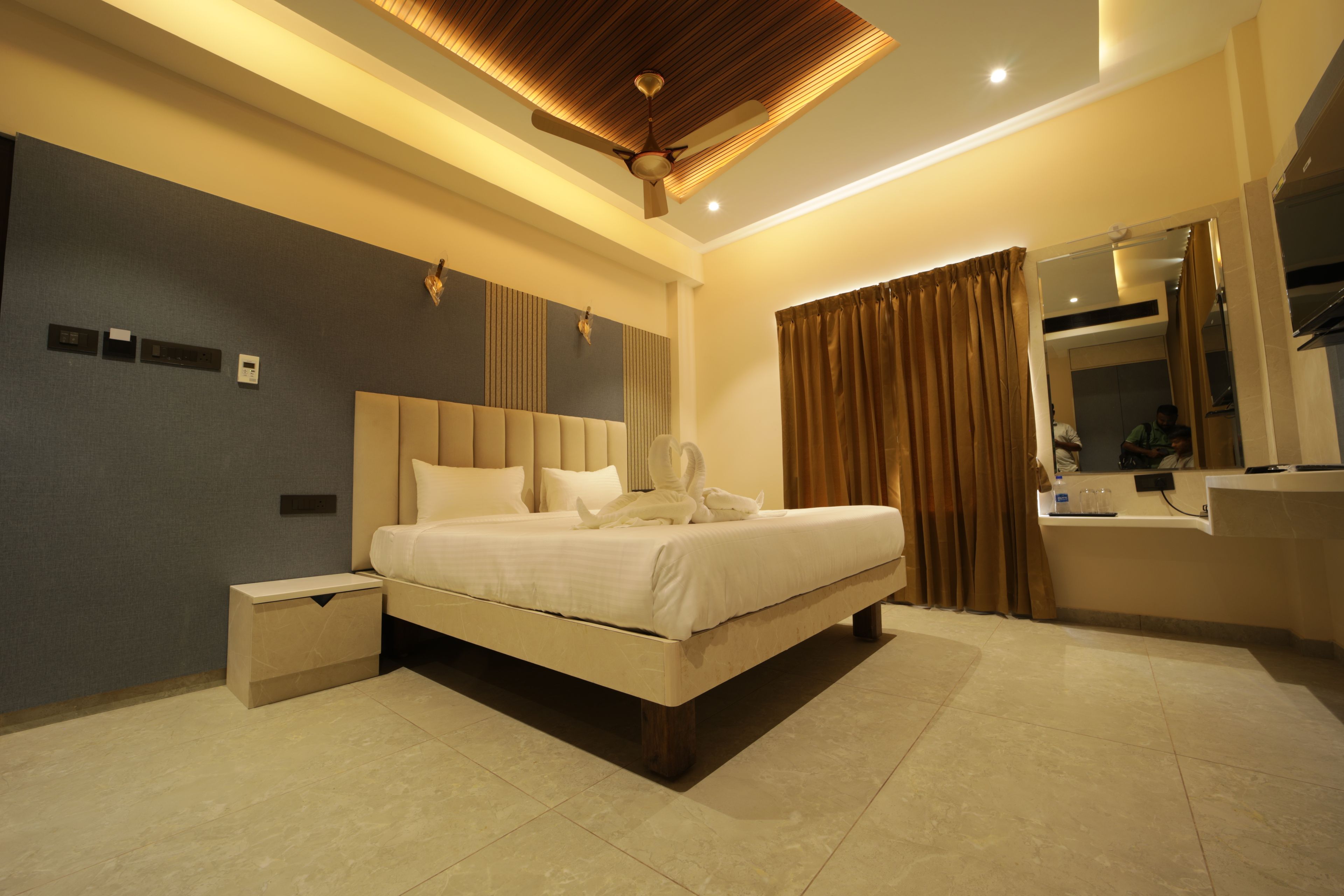 Un dormitorio moderno con una cama grande, una mesita de noche, un ventilador de techo y un baño con espejo y lavamanos.