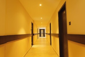 Pasillo de hotel con puertas a ambos lados, piso de baldosas e iluminación empotrada en el techo.