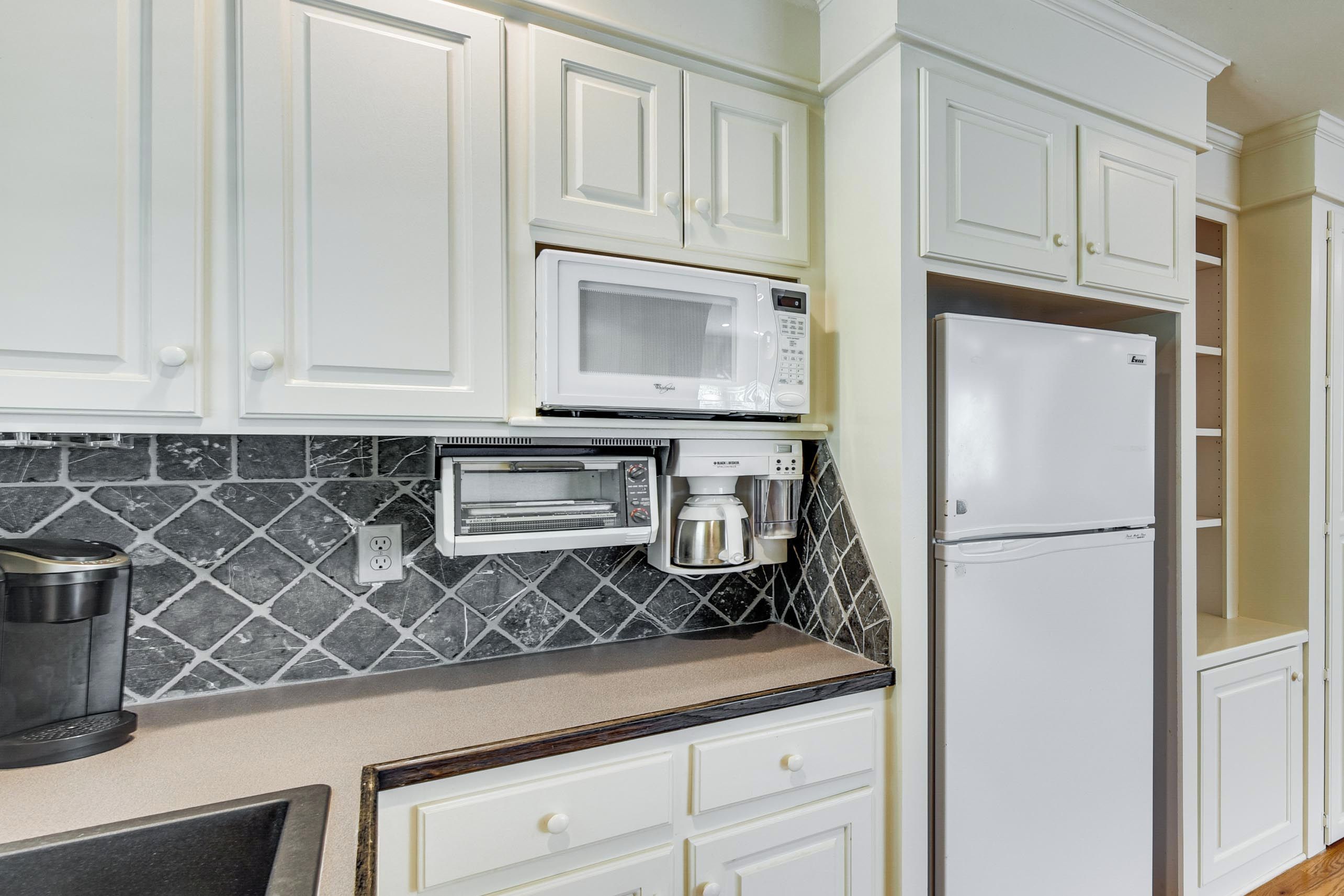 A kitchen with white cabinets, a microwave, a toaster oven, a coffee maker, and a refrigerator.
