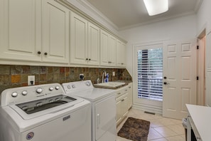 A kitchen with white cabinets, a stove, and a washing machine. There is a window with blinds and a door with a handle. - Dock, Hot Tub, Game Room! Lake Wateree Retreat (Camden)