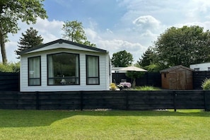 A single-story house with a gabled roof, a fenced yard, and a small shed in the background.