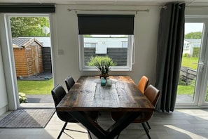 A dining area with a wooden table, six chairs, a potted plant, and a view of the backyard through a sliding door.