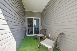 A small patio area with artificial grass, two wicker chairs, a small table, and a sliding glass door leading to a kitchen. - NMB Golf Retreat Near NMB Sports Complex (Little River)