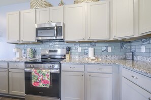 A kitchen with white cabinets, a stainless steel microwave, a stove, and a tiled backsplash. - NMB Golf Retreat Near NMB Sports Complex (Little River)