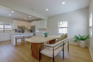 Een moderne keuken met witte kasten, een houten eiland met barkrukken, en een eetgedeelte met een bank en tafel.