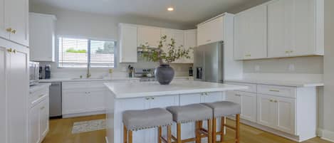 A modern kitchen with white cabinetry, a central island with stools, and a large window.