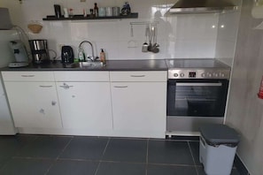 Une cuisine avec des meubles blancs, une cuisinière, un évier et une poubelle.