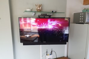 Un téléviseur à écran plat fixé au mur, avec une étagère en verre au-dessus.
