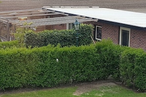Un bâtiment en briques doté d’un espace extérieur abrité, d’une haie verdoyante et d’un lampadaire.
