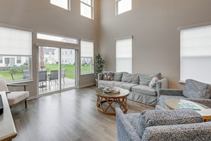 Ein geräumiges Wohnzimmer mit einer großen Schiebetür zu einer Terrasse, einem grauen Sofagarnitur, einem runden Couchtisch und einem gemusterten Sessel.