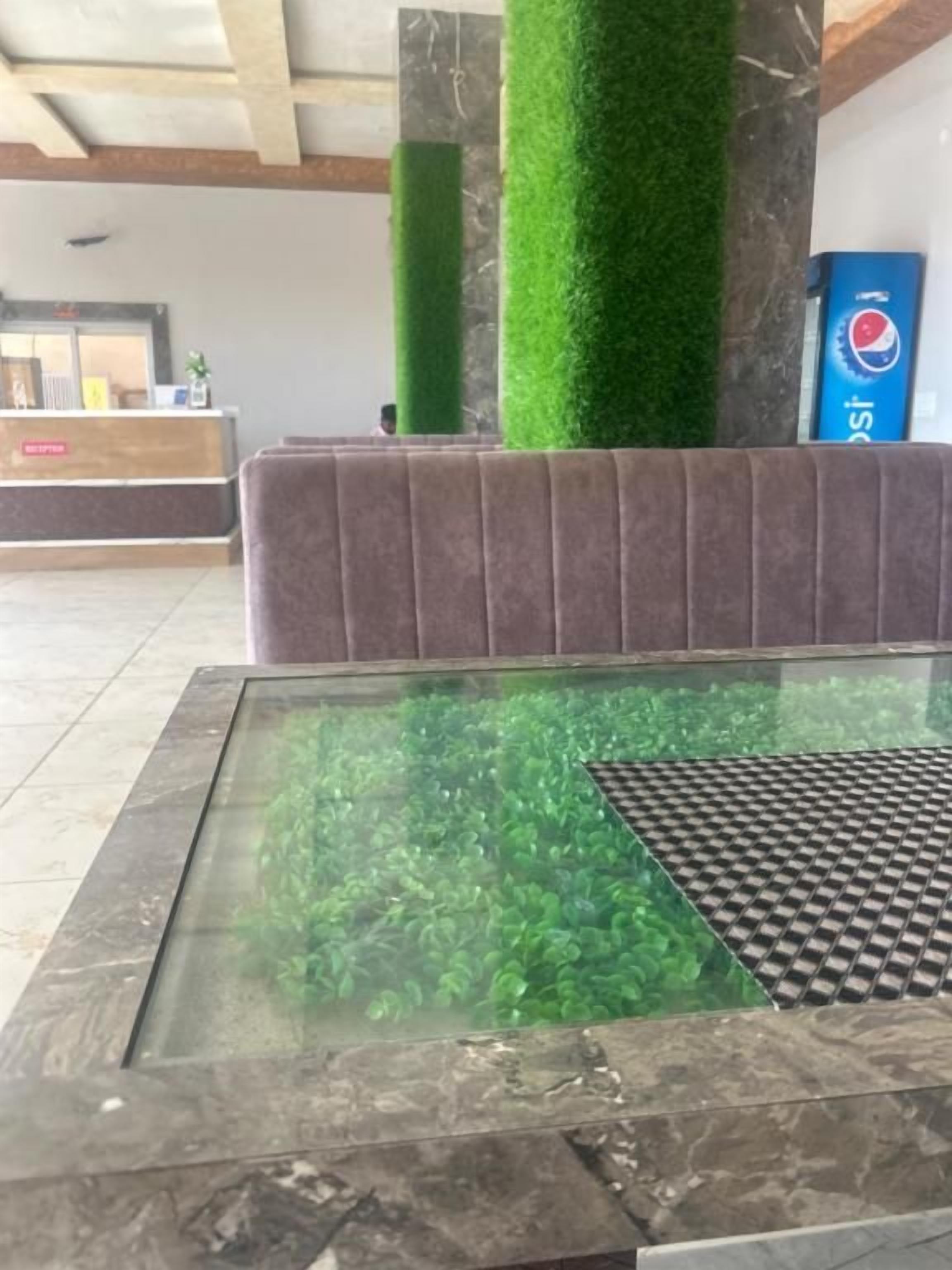 Un área de recepción con mostrador, una mesa de vidrio con plantas verdes y una máquina expendedora de Pepsi.