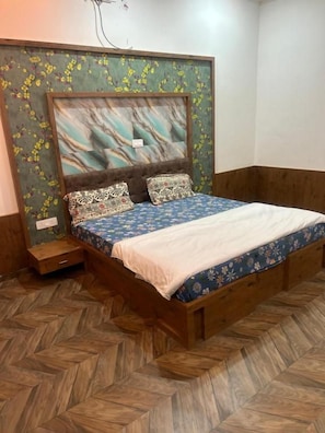 A bed with a wooden frame, a patterned bedspread, and two decorative pillows. - SHREE RADHE PALACE (Degana)