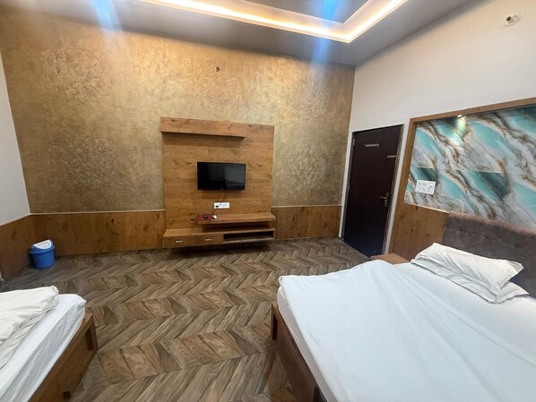 Une chambre d’hôtel avec deux lits, un téléviseur fixé sur un mur recouvert de panneaux en bois, et un parquet à motifs en chevrons.