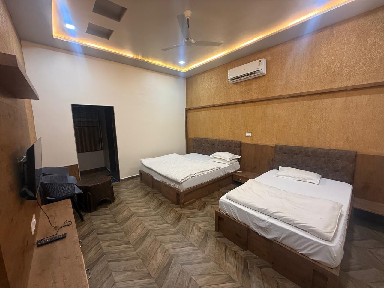 A room with two beds, a desk with a computer, and a ceiling fan.