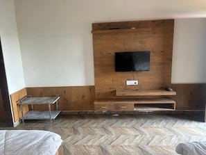 A room with a wooden wall unit, a flat-screen TV mounted on it, and a small metal shelf. - SHREE RADHE PALACE (Degana)
