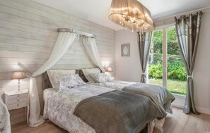 Ein Schlafzimmer mit Himmelbett, Nachttischlampen, einem großen Fenster mit Vorhängen und einem Kronleuchter.