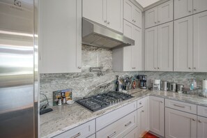 A modern kitchen with white cabinets, a stainless steel range hood, and a marble countertop. - Play & Unwind! Pass Christian Home < 1 Mi to Gulf (Pass Christian)