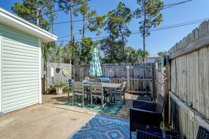 A backyard with a patio table and chairs, surrounded by a wooden fence and various plants. - Beach Days + Chartered Boat Tours! PCB Retreat (Panama City Beach)