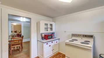 A compact kitchen with white cabinetry, a red microwave, and a white stove.