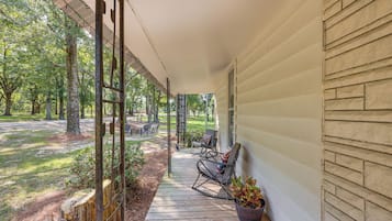 A covered porch with outdoor seating, a wooden deck, and a view of a wooded area.